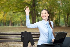 businesswoman working in park and waving hello
